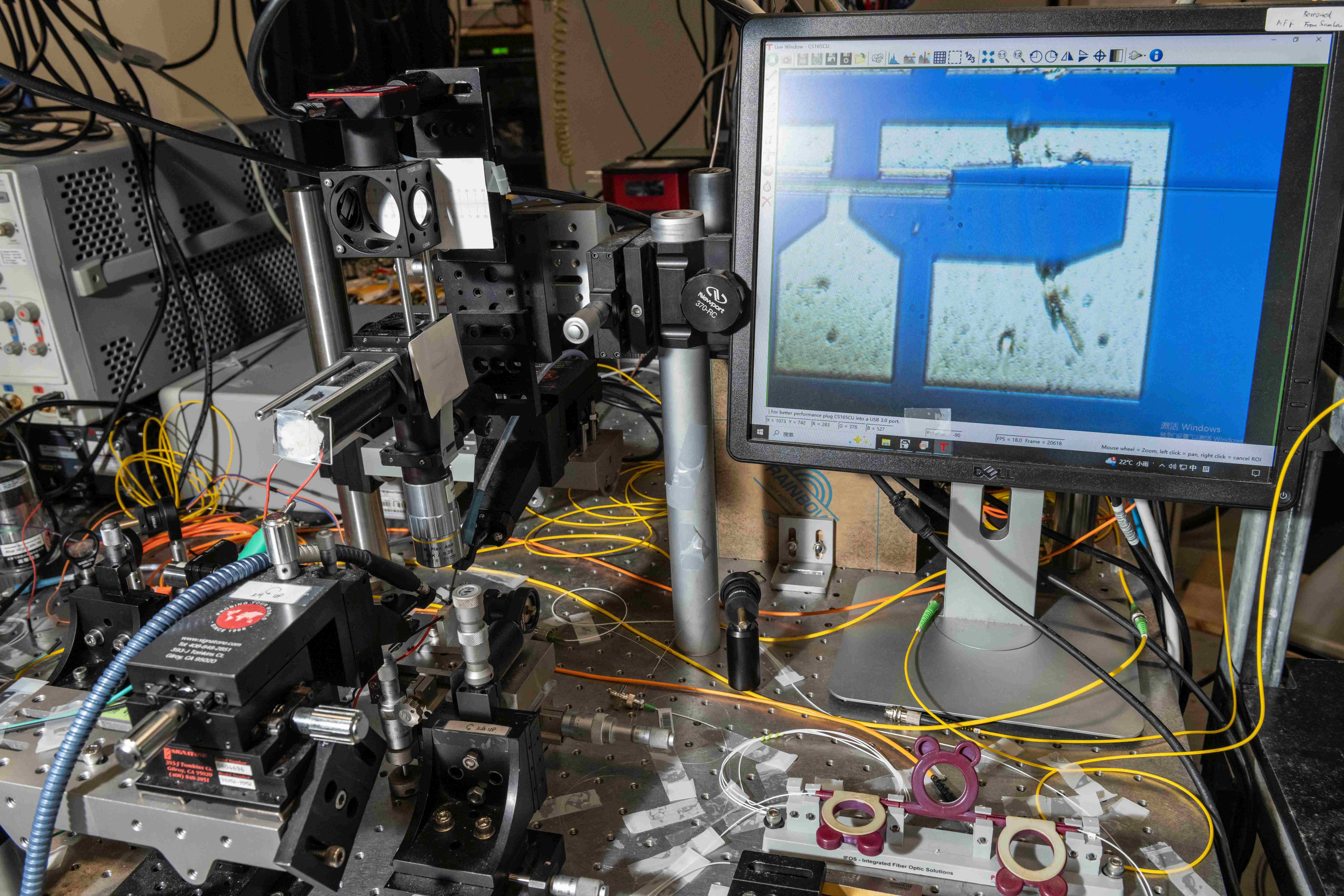 团队利用显微镜观察芯片，右边屏幕展示了锗离子注入的硅波导光电二极管探测器。